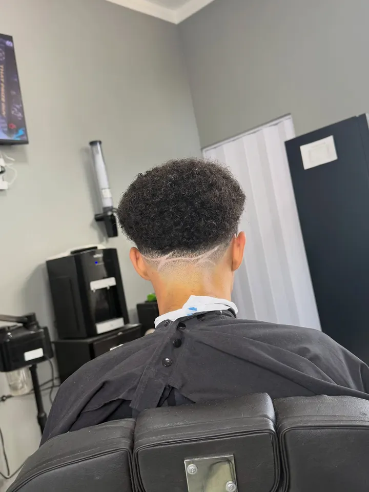 Corte cacheado com degradê e risco na nuca, visto de costas
